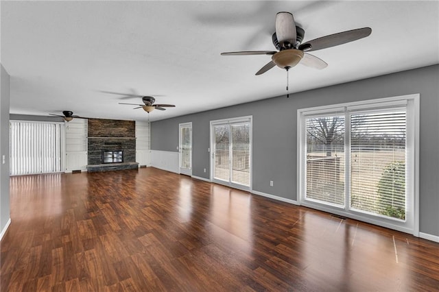 unfurnished living room with ceiling fan, baseboards, a stone fireplace, and wood finished floors