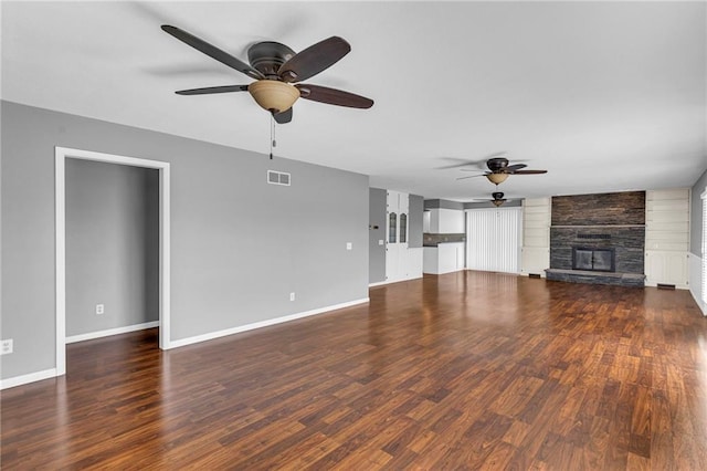 unfurnished living room with wood finished floors, visible vents, baseboards, a ceiling fan, and a stone fireplace