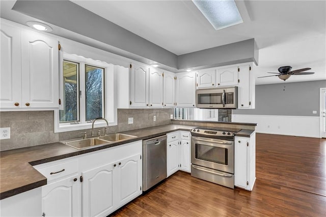 kitchen featuring dark countertops, white cabinets, stainless steel appliances, and a sink