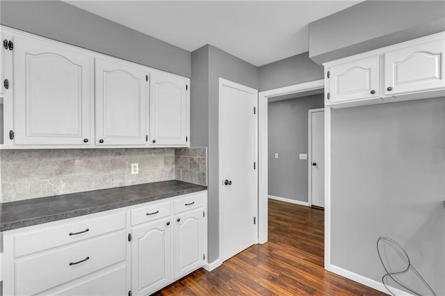 kitchen with backsplash, dark countertops, dark wood finished floors, white cabinetry, and baseboards