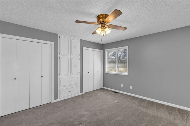 unfurnished bedroom with baseboards, ceiling fan, carpet, multiple closets, and a textured ceiling