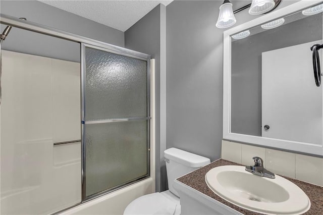 bathroom with vanity, toilet, shower / bath combination with glass door, and a textured ceiling