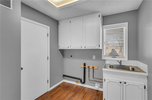 washroom featuring visible vents, dark wood-type flooring, cabinet space, electric dryer hookup, and a sink