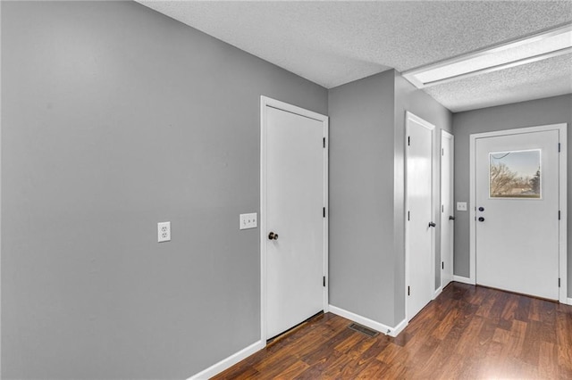 foyer entrance with visible vents, a textured ceiling, baseboards, and wood finished floors