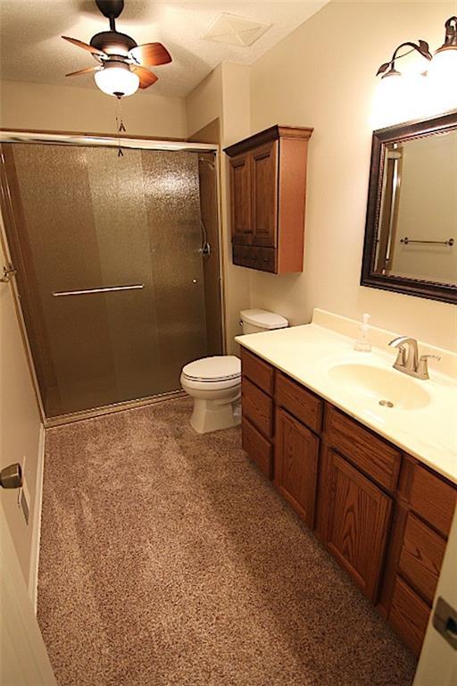 225 N Woodson Dr, Raymore, MO 64083 - full bathroom with toilet, a ceiling fan, a textured ceiling, vanity, and a stall shower