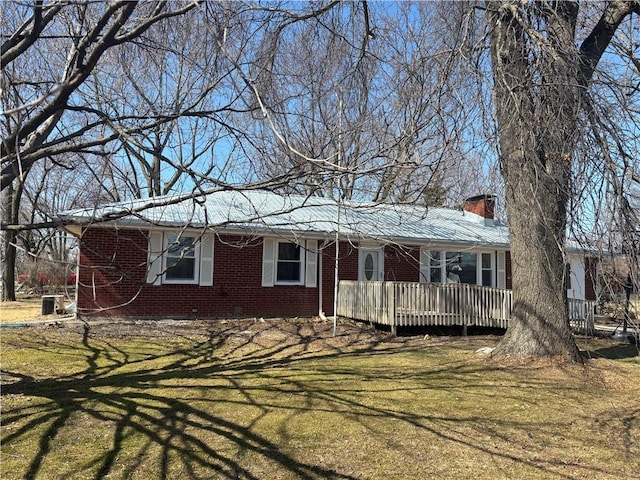 ranch-style house with a deck, a front lawn, brick siding, and a chimney