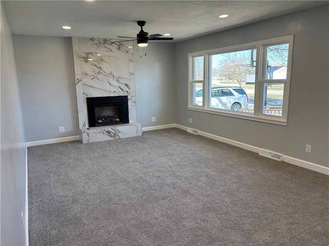 unfurnished living room featuring a premium fireplace, visible vents, baseboards, and dark colored carpet