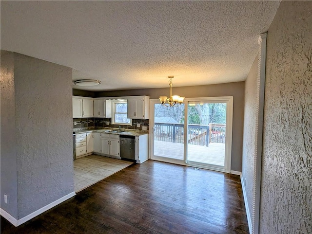 kitchen with a chandelier, a textured wall, wood finished floors, white cabinetry, and stainless steel dishwasher