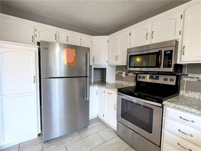 kitchen with a textured ceiling, white cabinetry, appliances with stainless steel finishes, light tile patterned flooring, and decorative backsplash