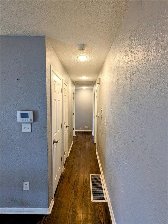 hallway featuring wood finished floors, a textured wall, visible vents, and a textured ceiling