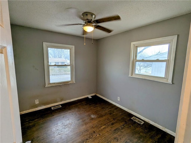 spare room with dark wood-style floors, visible vents, a ceiling fan, and baseboards