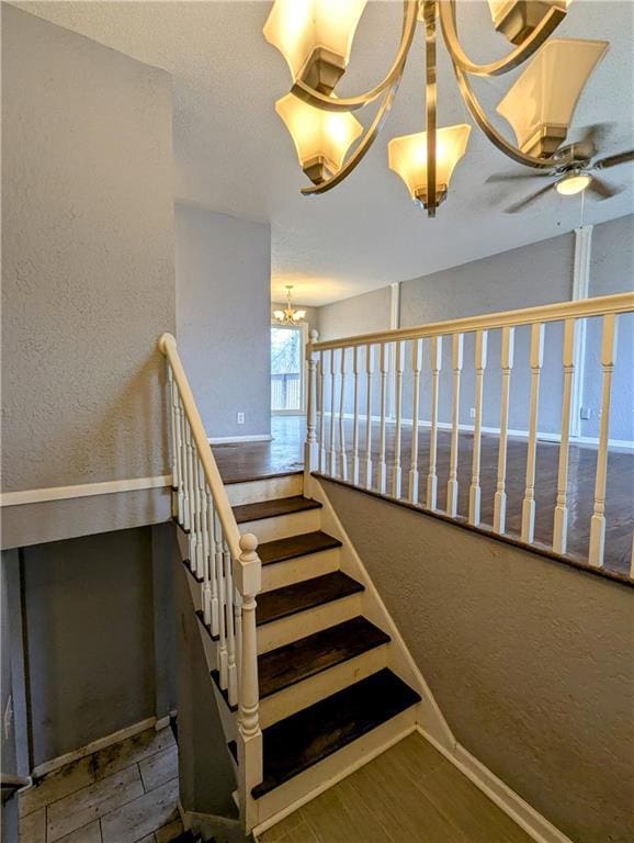 staircase featuring ceiling fan with notable chandelier, wood finished floors, a textured wall, and baseboards