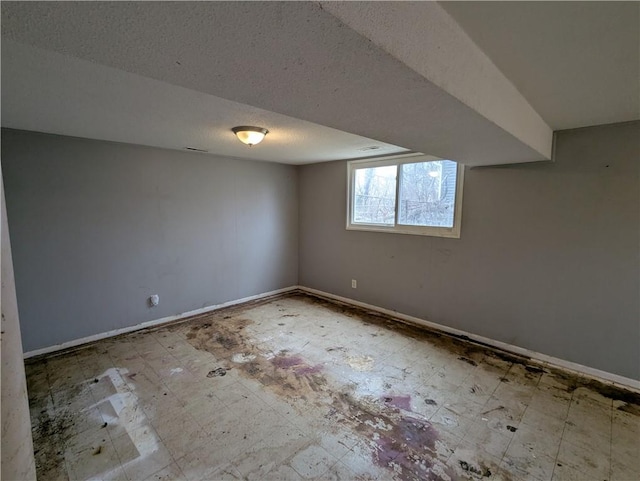 below grade area with tile patterned floors, a textured ceiling, and baseboards