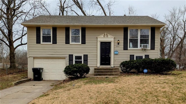 bi-level home featuring a front lawn, concrete driveway, an attached garage, and fence