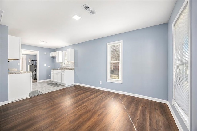 unfurnished living room with wood finished floors, visible vents, baseboards, water heater, and a sink