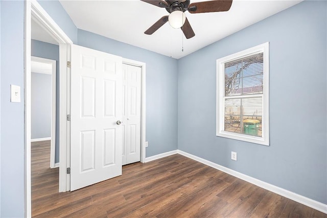 unfurnished bedroom featuring dark wood-style floors, a closet, baseboards, and a ceiling fan