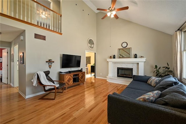 living area featuring ceiling fan, baseboards, a tile fireplace, light wood-style floors, and high vaulted ceiling