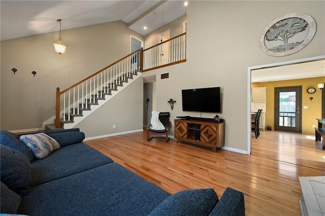 living area with stairway, baseboards, light wood-style floors, and high vaulted ceiling