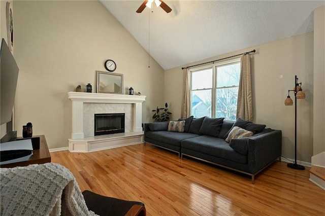 living area featuring a tile fireplace, baseboards, light wood-type flooring, and ceiling fan