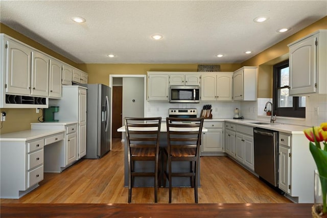 kitchen with light wood finished floors, a sink, tasteful backsplash, stainless steel appliances, and light countertops