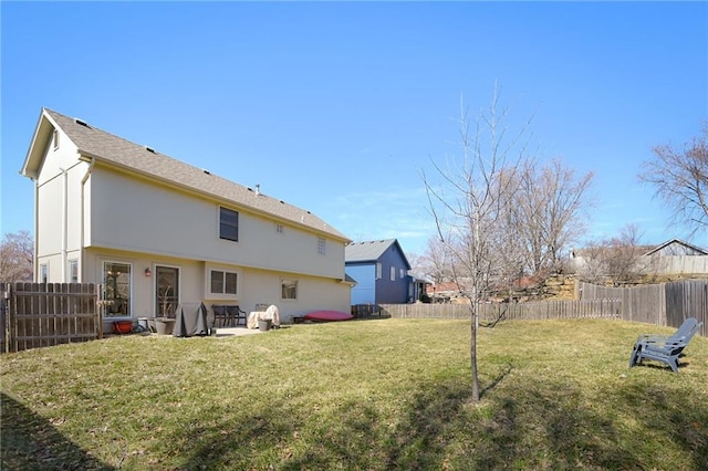 rear view of property featuring a lawn, a fenced backyard, and stucco siding