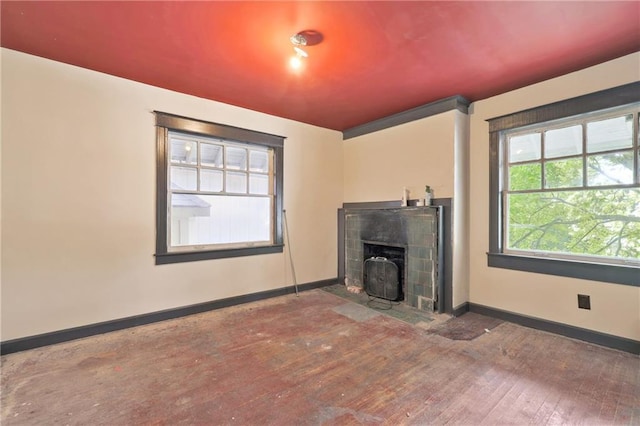 unfurnished living room featuring a tiled fireplace, baseboards, and wood-type flooring