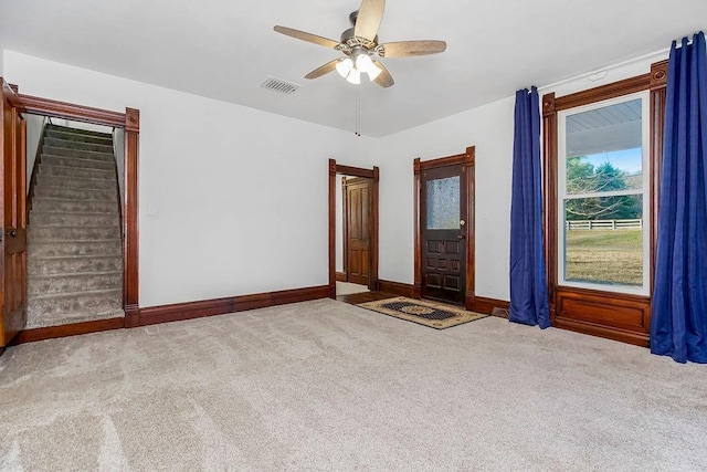 carpeted spare room featuring visible vents, baseboards, ceiling fan, and stairs