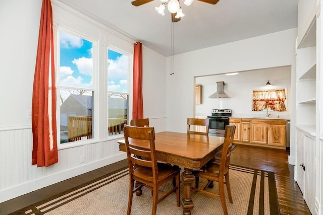 dining room with dark wood finished floors, a ceiling fan, and wainscoting