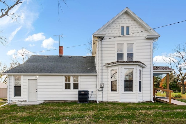 rear view of property featuring cooling unit, a yard, roof with shingles, and a chimney