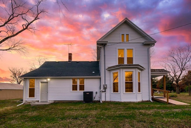 rear view of house featuring a yard, a shingled roof, and central AC