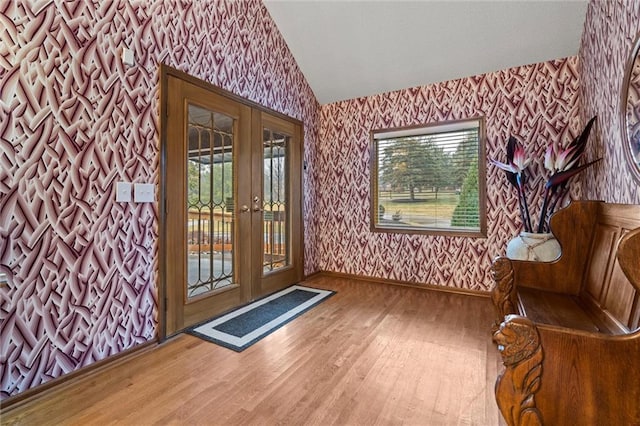 interior space with wood finished floors, french doors, wallpapered walls, baseboards, and vaulted ceiling