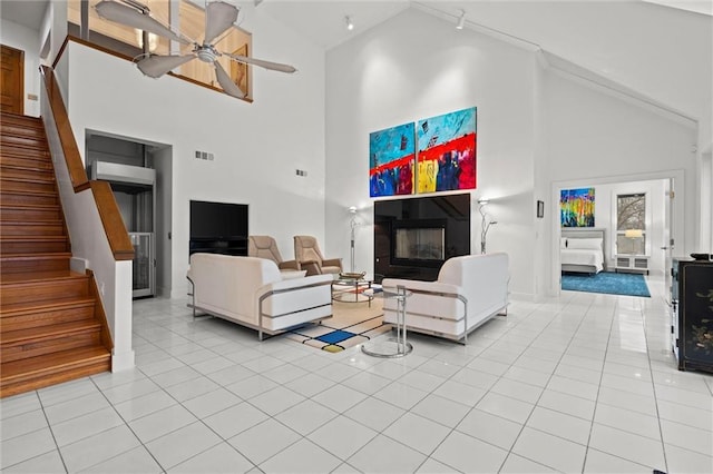 living room featuring light tile patterned floors, a ceiling fan, visible vents, stairs, and a glass covered fireplace