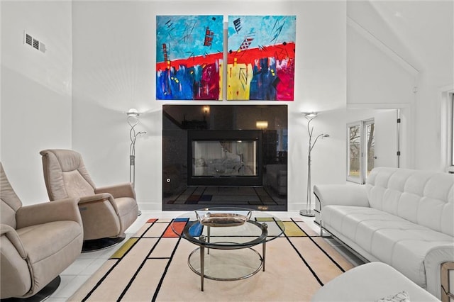 living area featuring a glass covered fireplace, baseboards, visible vents, and tile patterned flooring