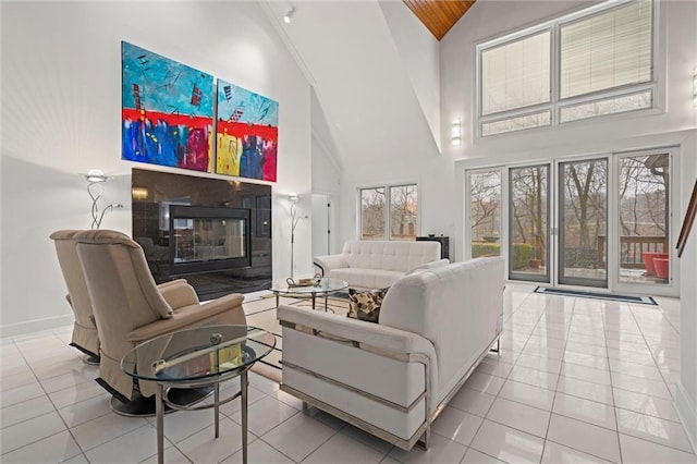 tiled living area featuring a glass covered fireplace, baseboards, and high vaulted ceiling