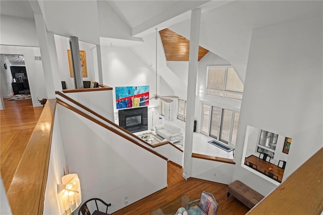 staircase with ceiling fan, wood finished floors, high vaulted ceiling, and a glass covered fireplace