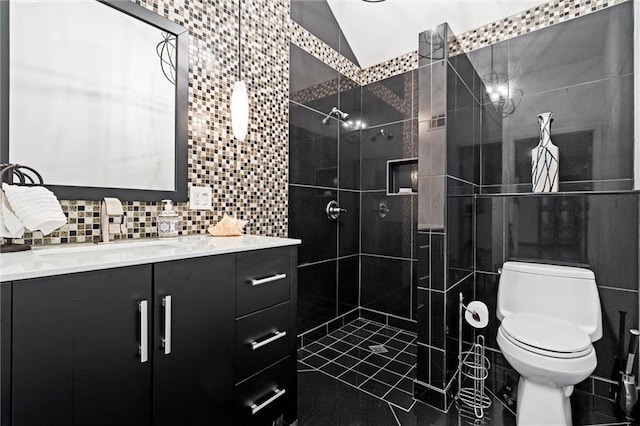 bathroom with toilet, vanity, vaulted ceiling, a tile shower, and tile walls