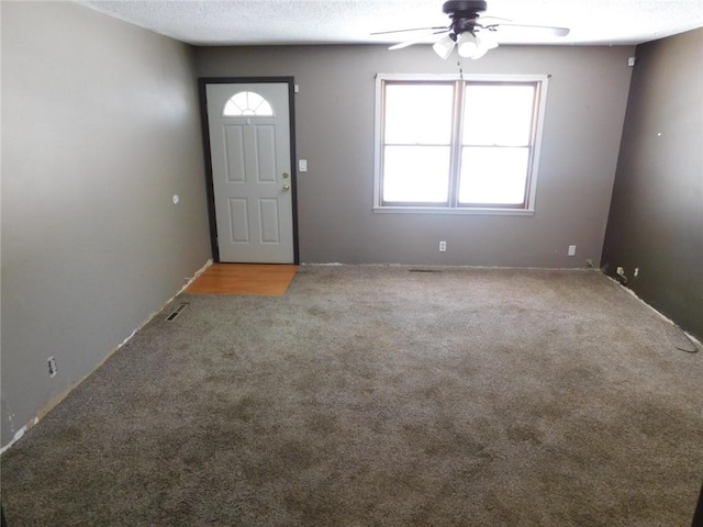 carpeted entryway featuring visible vents, a textured ceiling, and a ceiling fan