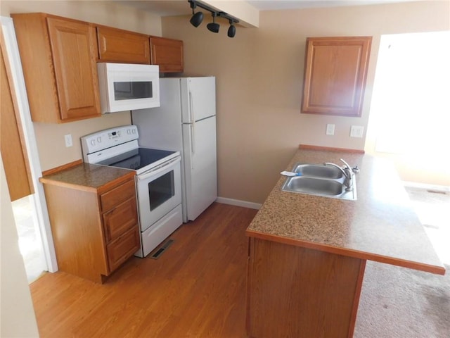 kitchen featuring white appliances, a peninsula, light wood-style floors, and a sink