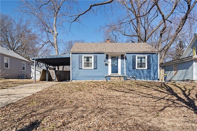 view of front of property with a carport, roof with shingles, concrete driveway, and a chimney