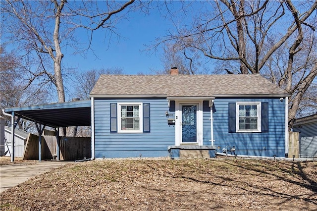 view of front of property featuring an attached carport, roof with shingles, concrete driveway, and a chimney