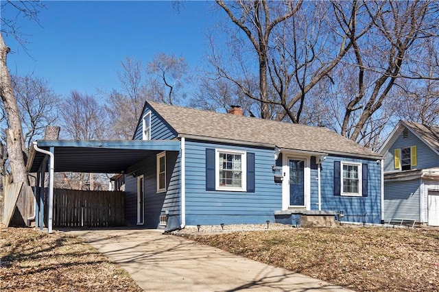 view of front facade with an attached carport, fence, concrete driveway, roof with shingles, and a chimney