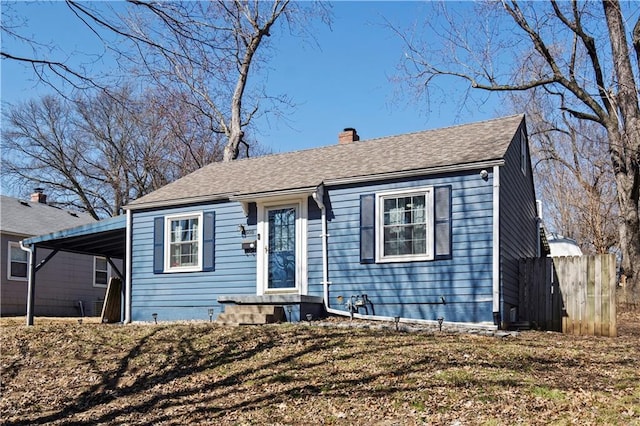 bungalow-style home featuring an attached carport, a shingled roof, a chimney, and fence