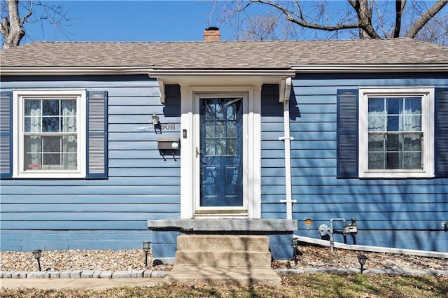 doorway to property featuring a chimney and a shingled roof