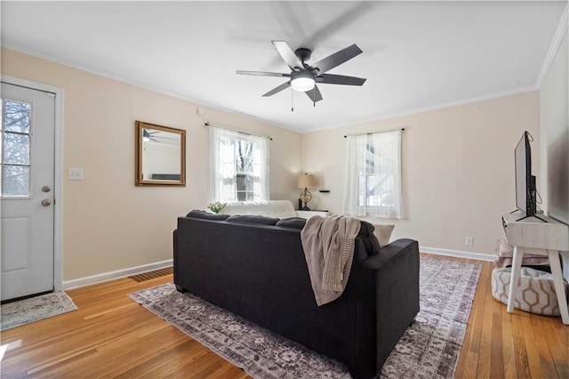 living area featuring light wood-type flooring, visible vents, ornamental molding, a ceiling fan, and baseboards