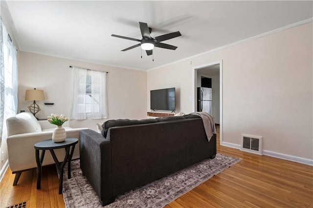 living area with visible vents, crown molding, baseboards, wood finished floors, and a ceiling fan