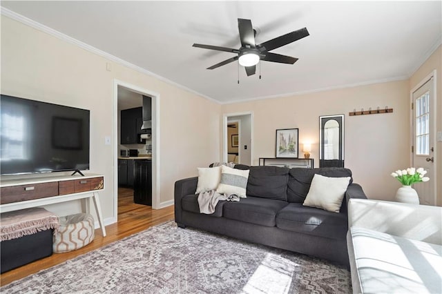 living room featuring baseboards, a ceiling fan, wood finished floors, and crown molding