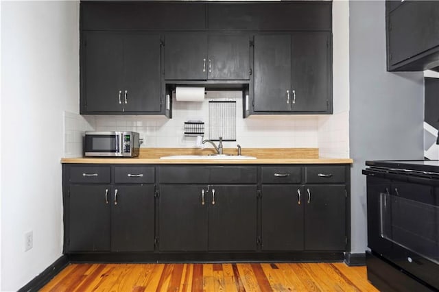 kitchen featuring light wood-style flooring, a sink, light countertops, black range oven, and stainless steel microwave