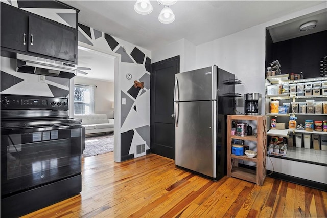 kitchen with black electric range oven, freestanding refrigerator, light wood-style floors, extractor fan, and dark cabinets