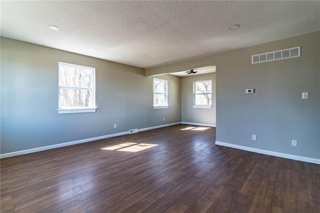 spare room with dark wood finished floors, visible vents, and baseboards