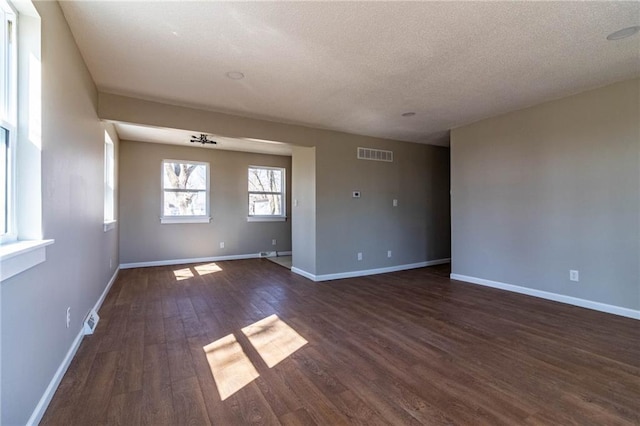 empty room featuring dark wood-style floors, visible vents, a textured ceiling, and baseboards